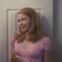 a woman in a pink dress is holding a glass and looking at the camera while standing next to a door