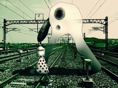 a person standing on train tracks next to a giant white object with black dots in it's eyes