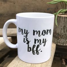 a white coffee mug with the words my mom is my bee on it next to a potted plant