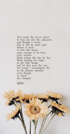 some yellow flowers are in a vase on a white table and there is a poem above it