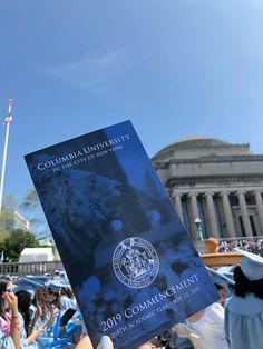 a person holding up a copy of the columbia university commencement program in front of an american flag