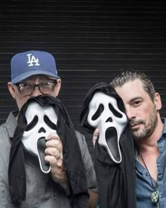 two men are holding up masks with faces painted on them