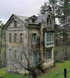 an old abandoned house sitting in the middle of a green field with trees around it