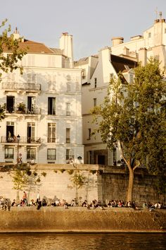 many people are sitting on the side of a building by the water in front of it