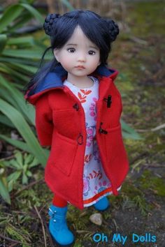 a doll is standing in the grass wearing a red coat and blue boots with her hair pulled back