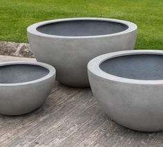 three cement planters sitting on top of a wooden table in front of some grass