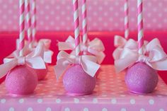 four pink cake pops with white bows and candles on a polka dot tablecloth background