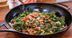 a pan filled with greens and bacon on top of a wooden table