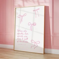 a pink wall with a white framed poster on the floor in front of it that says, when she speaks, her words are made & full of kindness