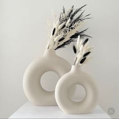 two white vases with black and white feathers in them