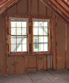 an attic with wooden walls and windows in the corner, next to a box on the floor