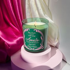 a green candle sitting on top of a white table next to pink and white curtains