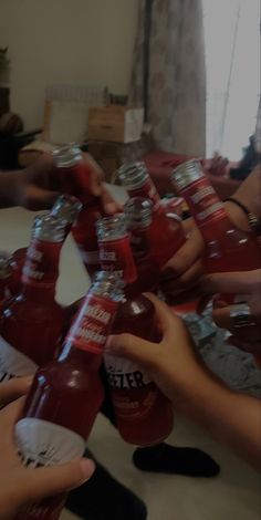 many people are holding up bottles of red liquid in front of each other on a table