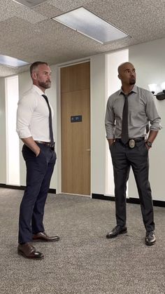 two men standing in an empty room with one wearing a tie and the other without