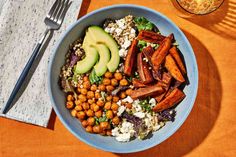 a blue bowl filled with vegetables and chickpeas next to a fork, knife and napkin