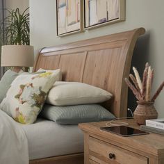 a bed with pillows on top of it next to a night stand and two framed pictures