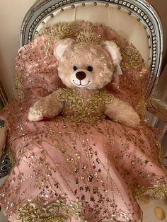 a teddy bear sitting on top of a bed in a pink and gold dress with sequins