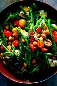 a bowl filled with green beans, tomatoes and chickpeas on top of a table