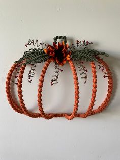 an orange string pumpkin is hanging on the wall next to another piece of art that looks like it has been made out of yarn