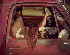 a woman sitting in the back seat of a red truck with her hand on the door handle