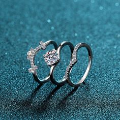 two silver rings with diamonds on them sitting on a blue surface, one has a diamond in the middle