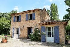 an old stone house with blue shutters on the front and side doors, surrounded by greenery