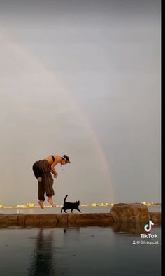 a person jumping in the air with a cat and a rainbow in the sky behind them