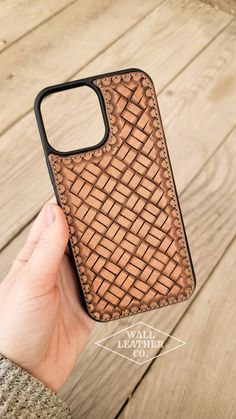 a hand holding an iphone case made out of brown woven material on wooden planks