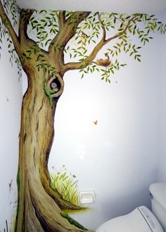 a bathroom with a tree painted on the wall and toilet in the corner next to it