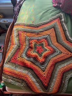 a crocheted blanket on top of a bed with pillows and blankets around it