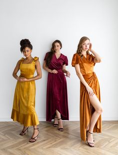 three women in different colored dresses standing next to each other on a wooden floor with white walls behind them