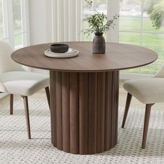 a round table with two chairs and a vase on it in front of a window