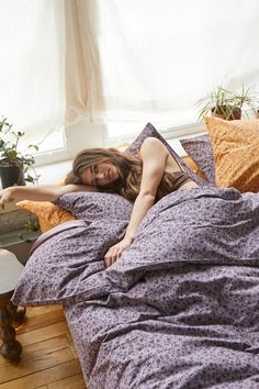 a woman is laying in bed with her legs up on the pillow and looking at the camera