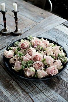 a plate full of pink roses sitting on top of a wooden table next to two candles