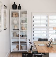 a room with white walls and wooden floors has a desk, chair, bookshelf, and window in it