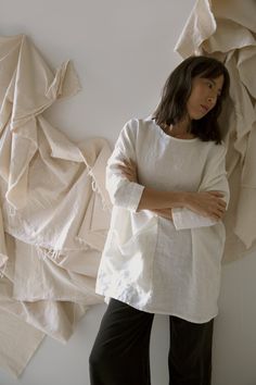 a woman standing next to a wall covered in white sheets and cloths with her arms crossed