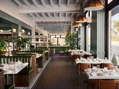 an empty restaurant with green booths and white tablecloths on the tables, along with potted plants