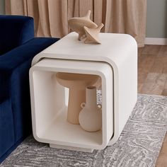 a white table with a vase on it in front of a blue couch and curtains