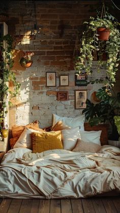 an unmade bed with lots of pillows and plants hanging from the brick wall behind it