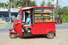 a man sitting in the back of a small red truck with bread on it's rack