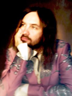 a man with long hair wearing a purple jacket