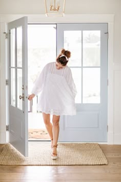 a woman walking into a door with her hand in her pocket and wearing a white dress