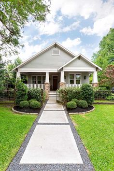 a house that is in the middle of some grass and bushes with trees around it