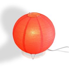 an orange paper lantern is sitting on a white surface with a wire attached to it