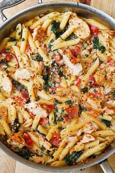 a pan full of pasta with chicken and spinach on top, sitting on a table