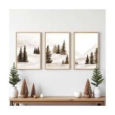 three paintings on the wall above a table with pine cones and fir trees in front of them