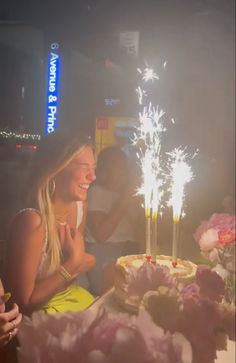 a woman sitting at a table with a cake and sparklers in front of her