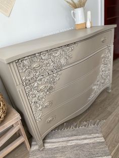 a white dresser sitting on top of a wooden floor next to a chair and vase