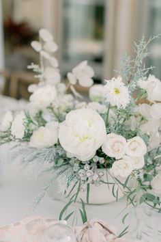 white flowers and greenery are arranged in vases on a dining room table with shells