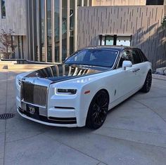 a white rolls royce parked in front of a building with black rims on it